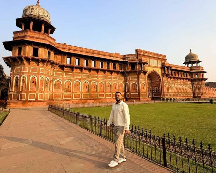 Traveler standing on the lawn in front of the red sandstone Jahangiri Mahal at Agra Fort, India